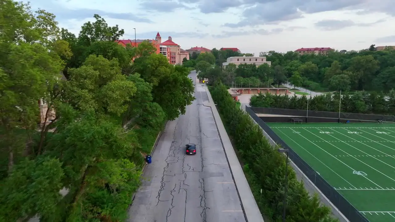 Aerial tracking shot of sedan car driving on college campus at sunset