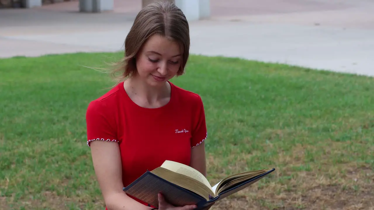 A student muses at the passage in a book while studying in the campus commons