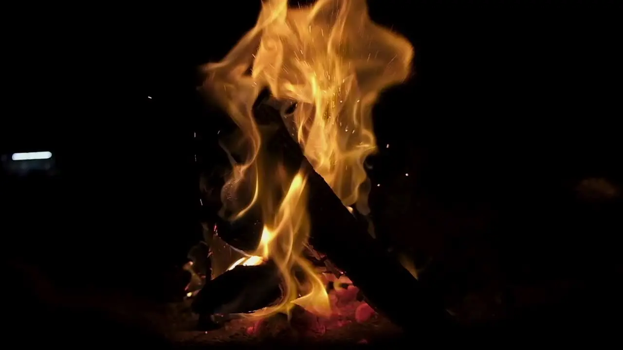 Wide shot of campfire burning in slowmotion black background bright hot flames burst in sparks