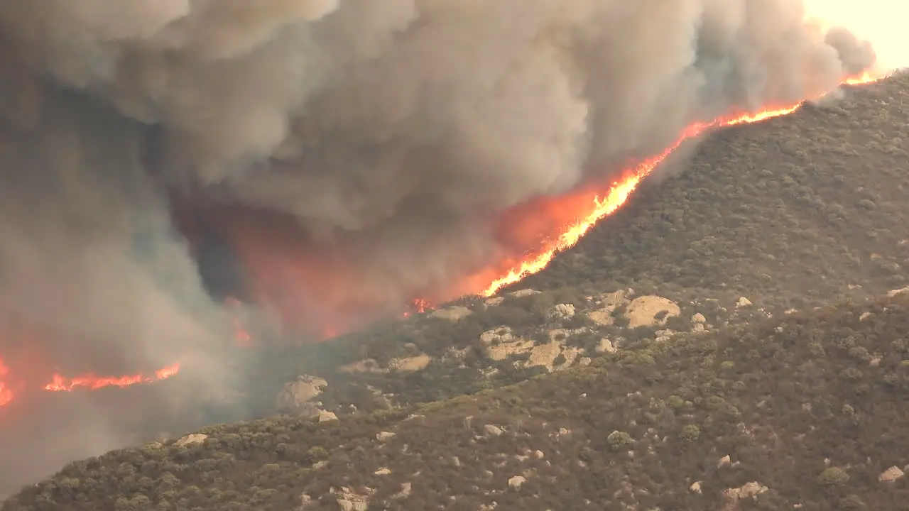 Large red hot flames crest over the ridgetop of a brush covered mountain in Hemet California