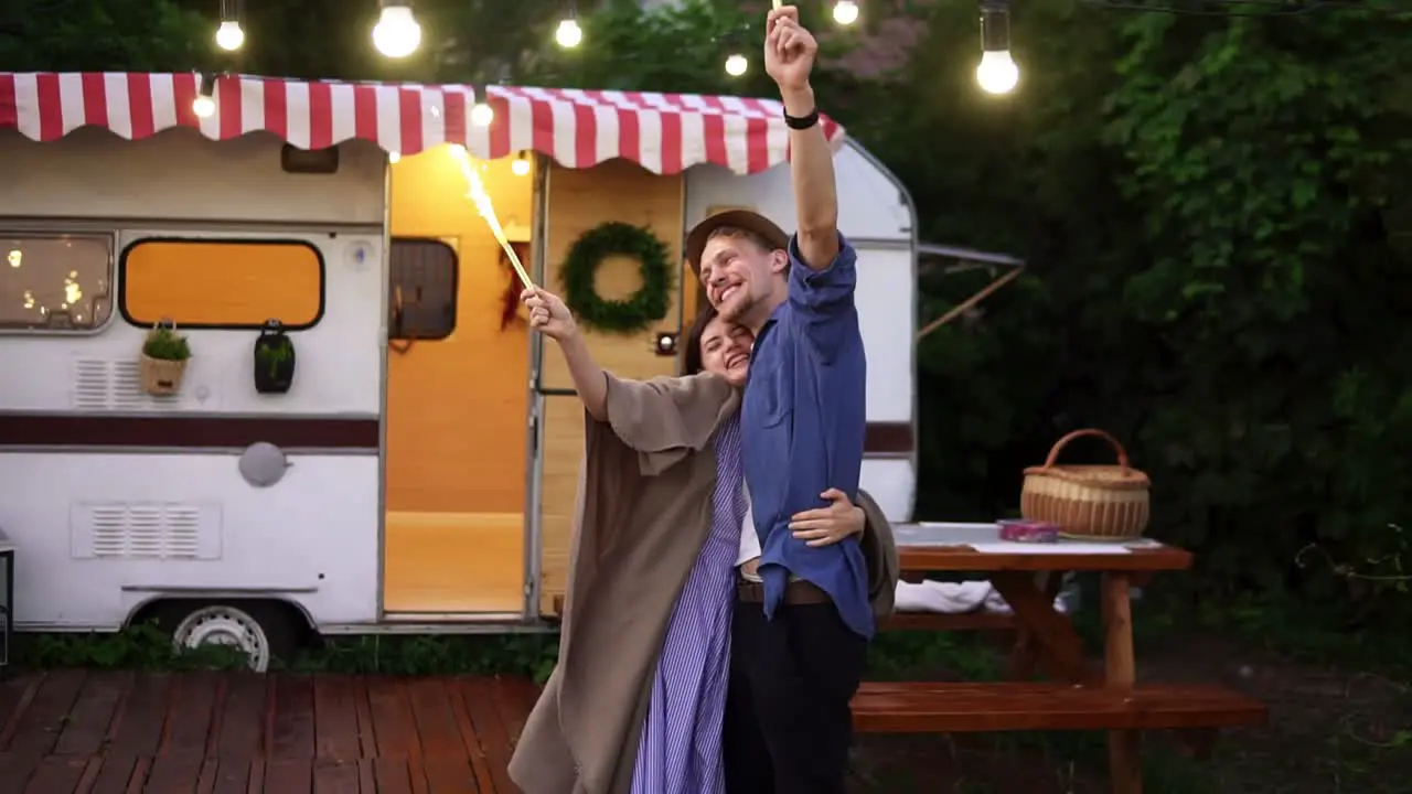 Young Couple Embracing Standing In Front Trailer They Living In With Sparklers Celebrating Dancing And Smiling