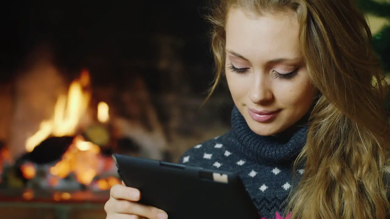 A young woman uses a tablet at the Christmas tree and fireplace 2