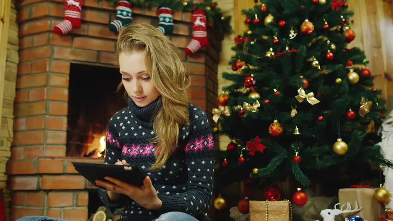 A young woman uses a tablet at the Christmas tree and fireplace