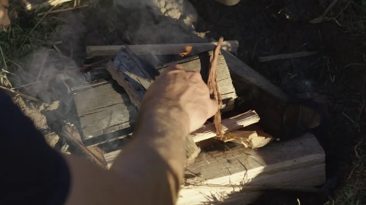 Placing kinderling on a smouldering smokey camp fire