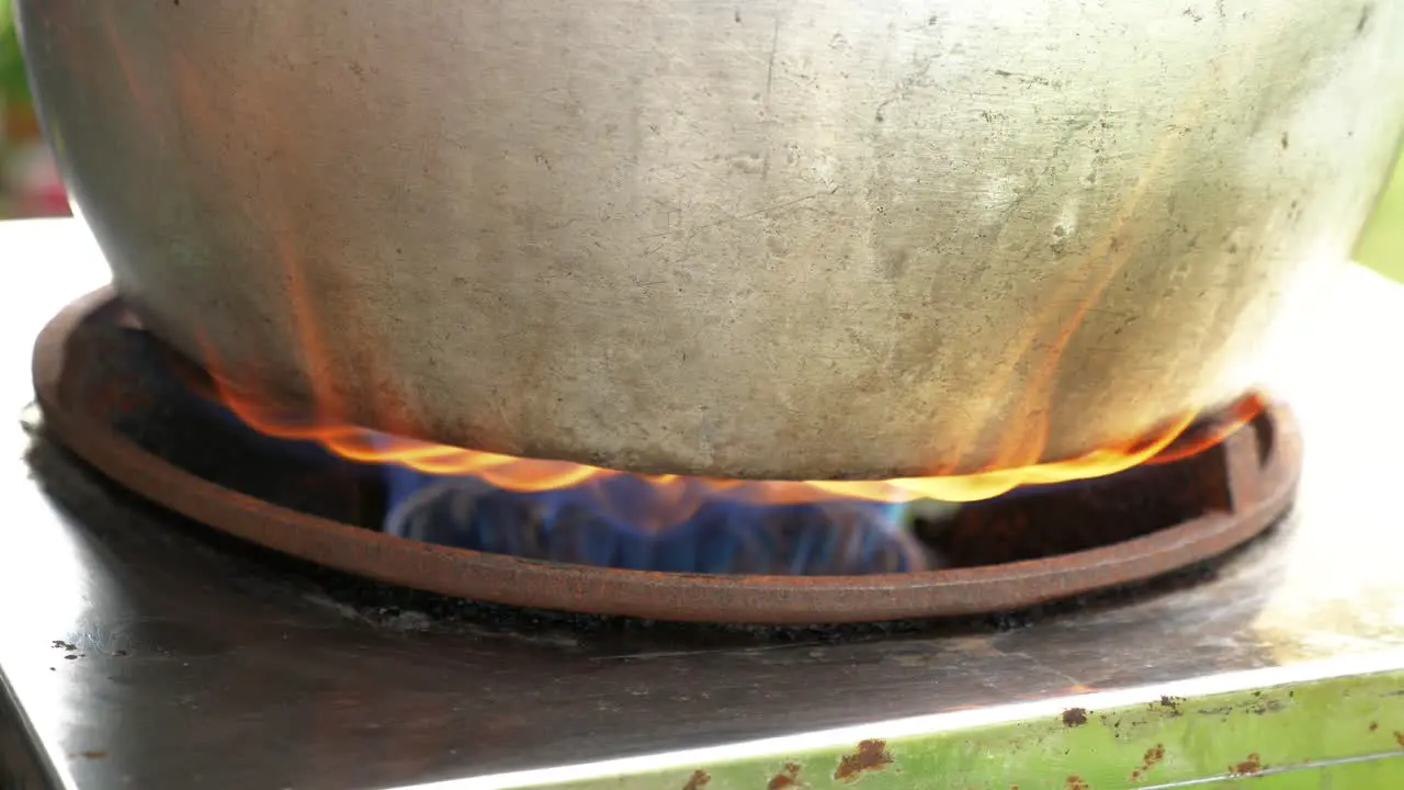 Stainless steel pot on burning flame boiling water close up handheld view