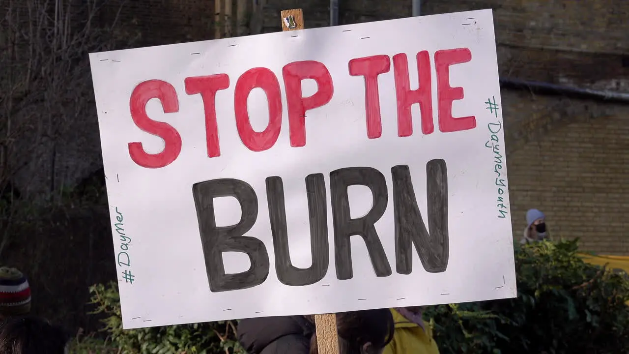 A handmade cardboard placard is held up that reads Stop the burn” at a protest opposing a new waste incinerator at Edmonton