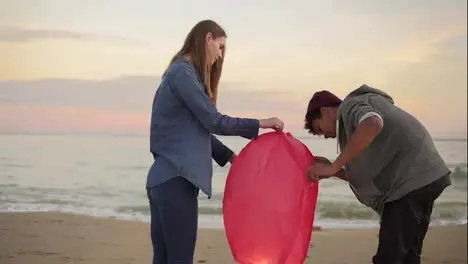 Young multi ethnic couple lightning red paper lantern before launching Romantic date on the beach Attractive woman holding