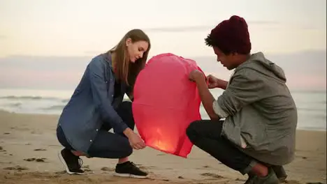 Romantic date at the beach during sunset Young multi ethnic couple holding red paper lantern before launching Attractive woman