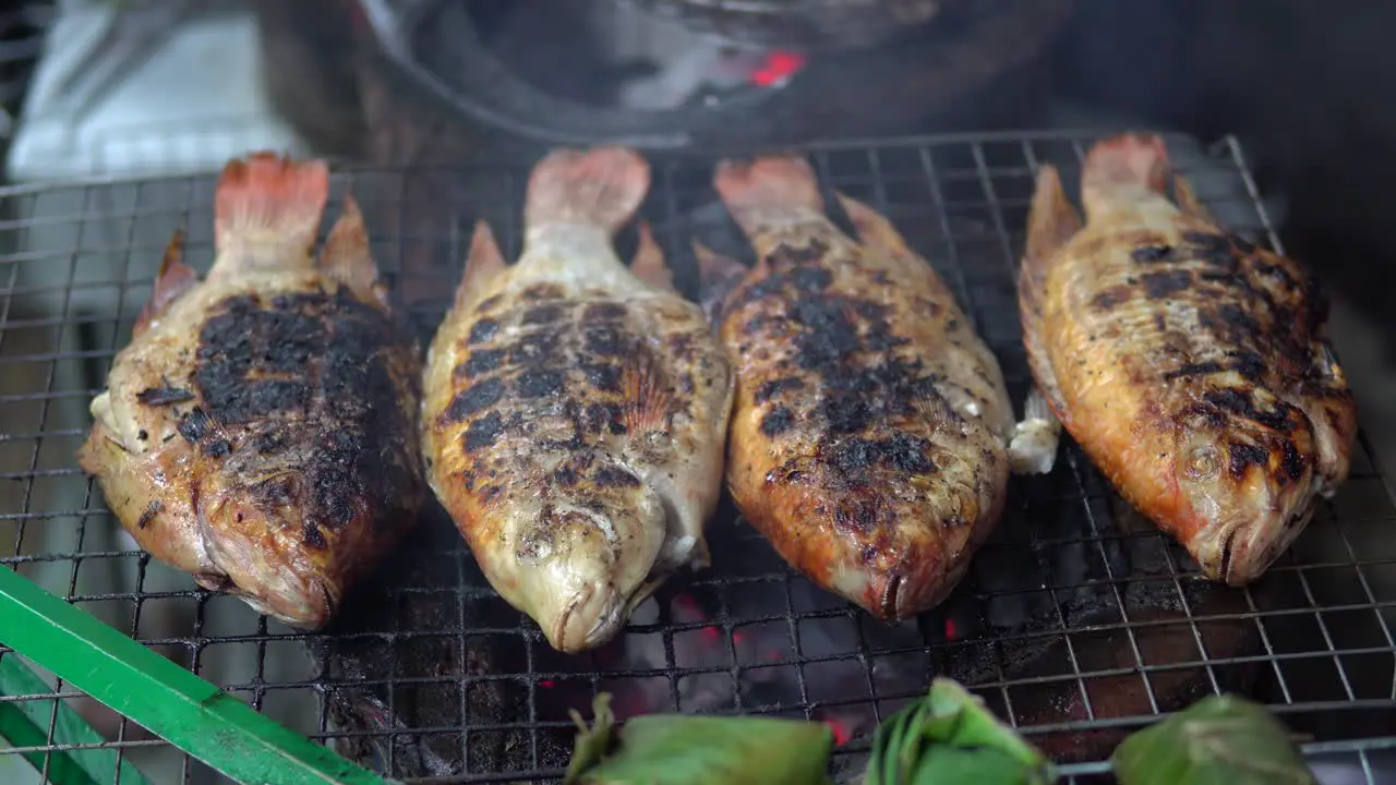 Whole Sea fish is being cooked on metal grid grill at the street near restaurant in Thailand