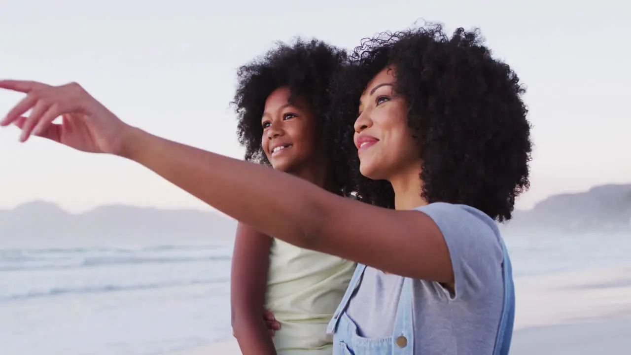 African american mother and daughter smiling looking at each other at the beach