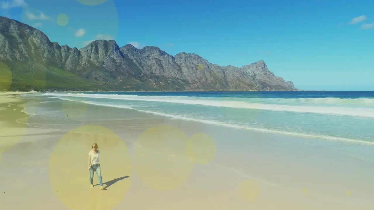 Multiple light spots floating against caucasian woman walking at the beach