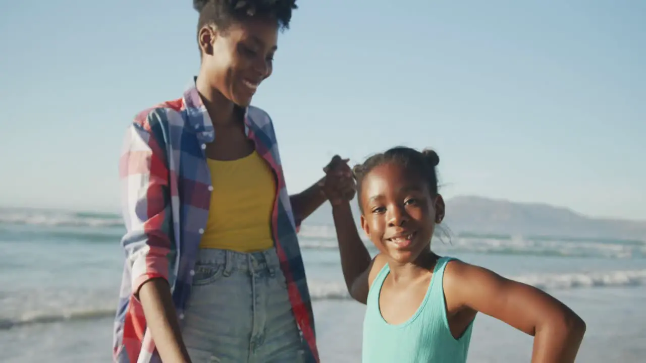 African american mother holding her daughter's hand and walking on the beach