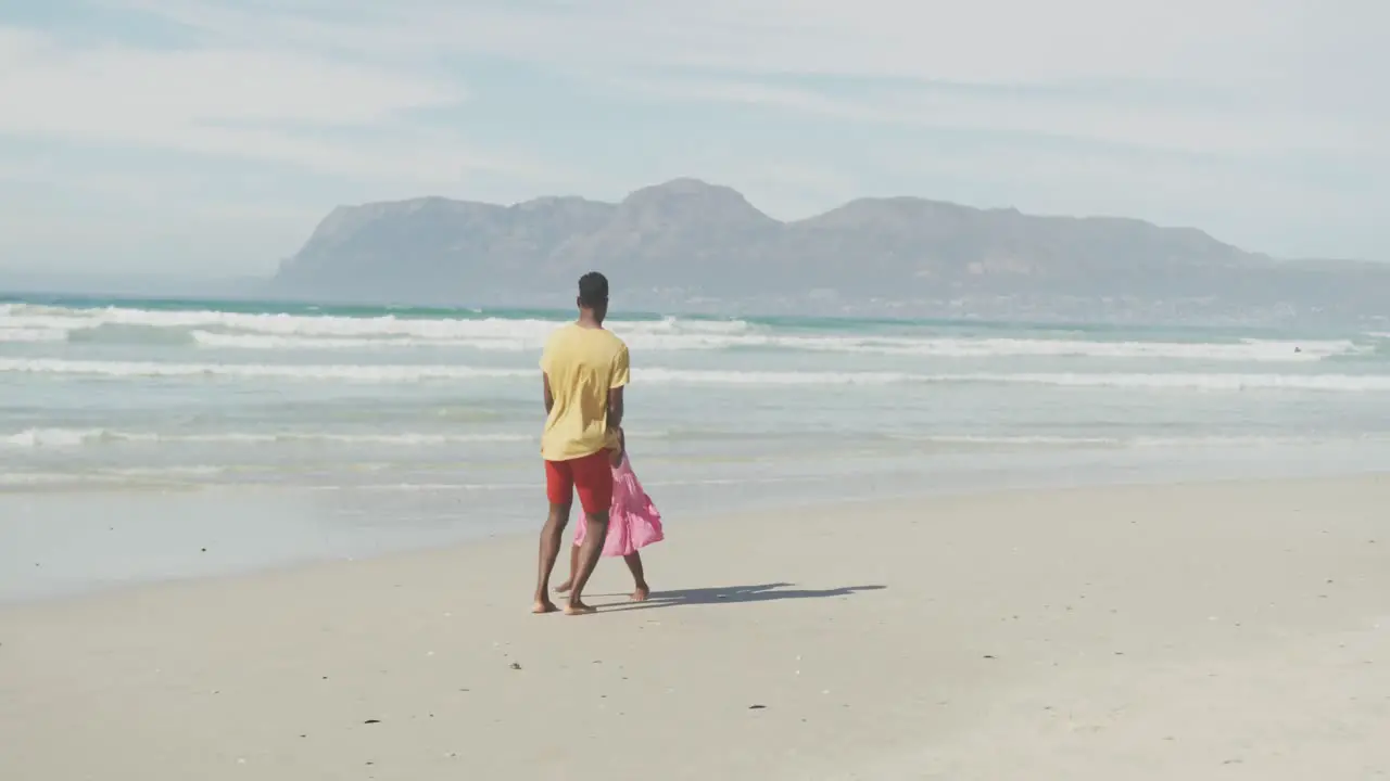 African american father and daughter holding hands jumping at the beach