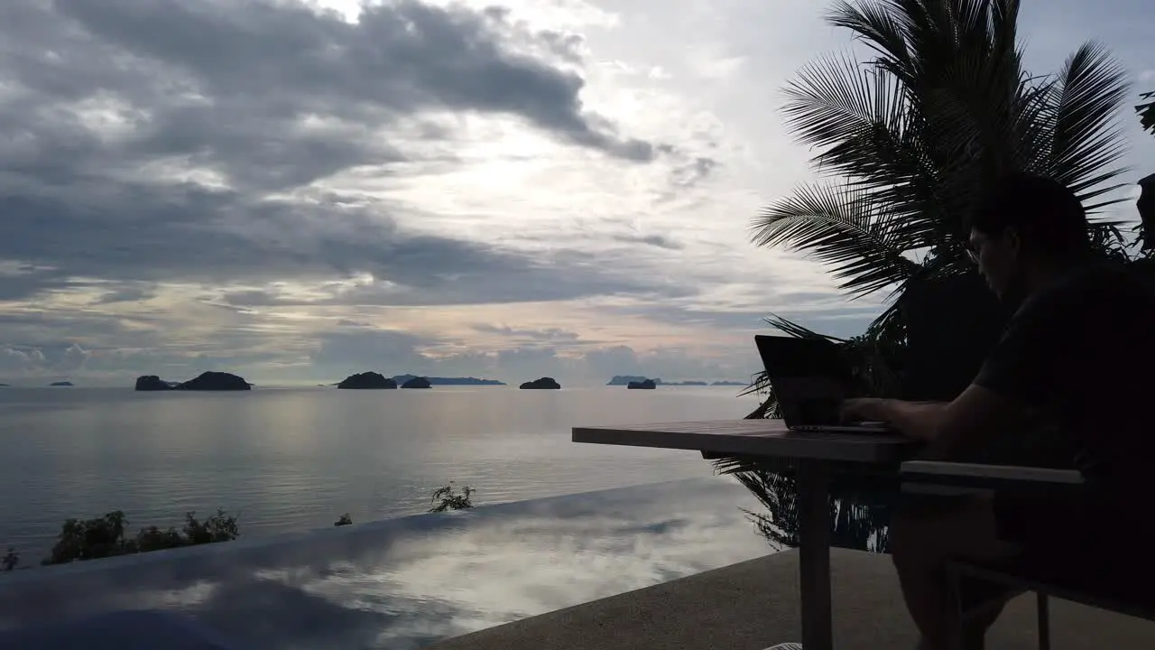 Asian man working on the laptop by the pool panning view