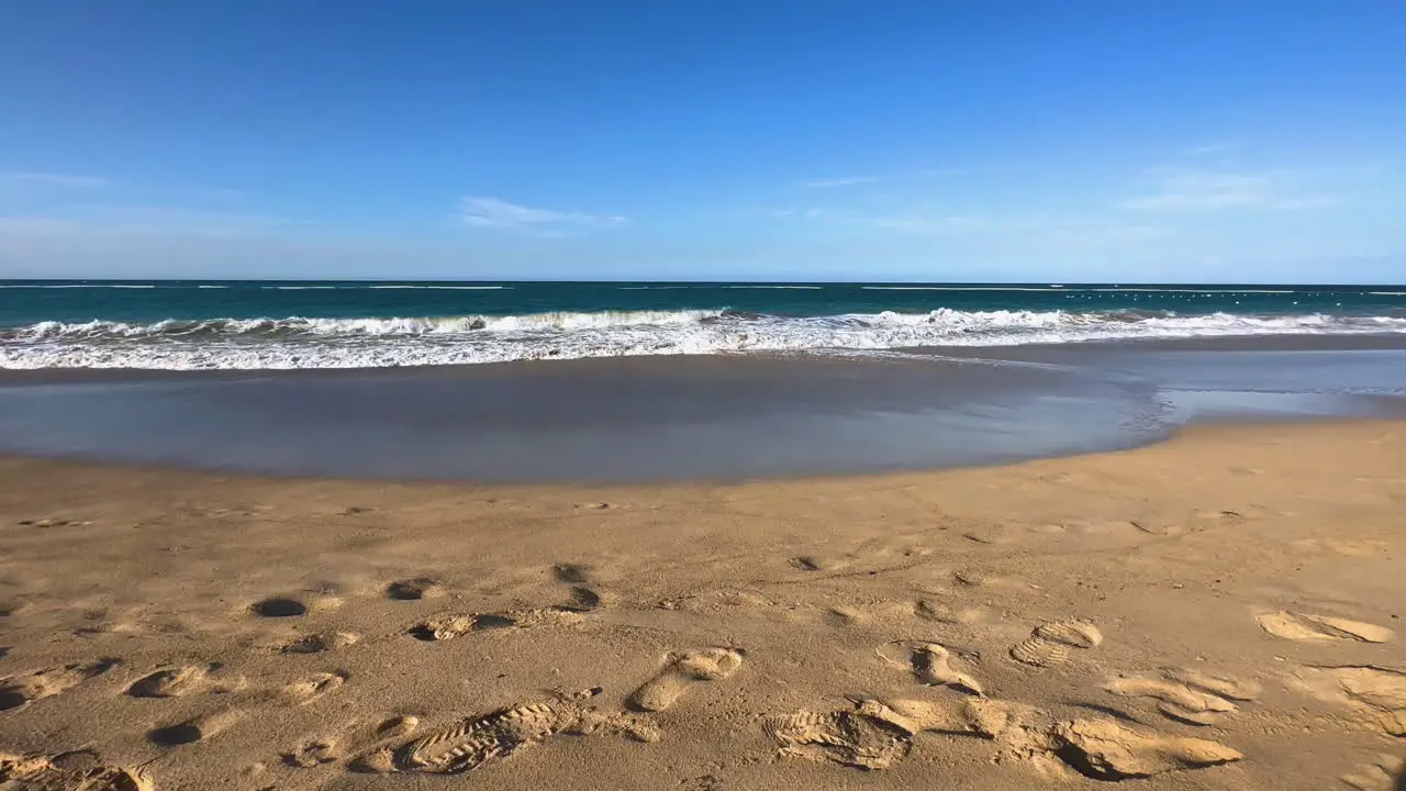 waves roll onto beach with sandy footsteps in the foreground