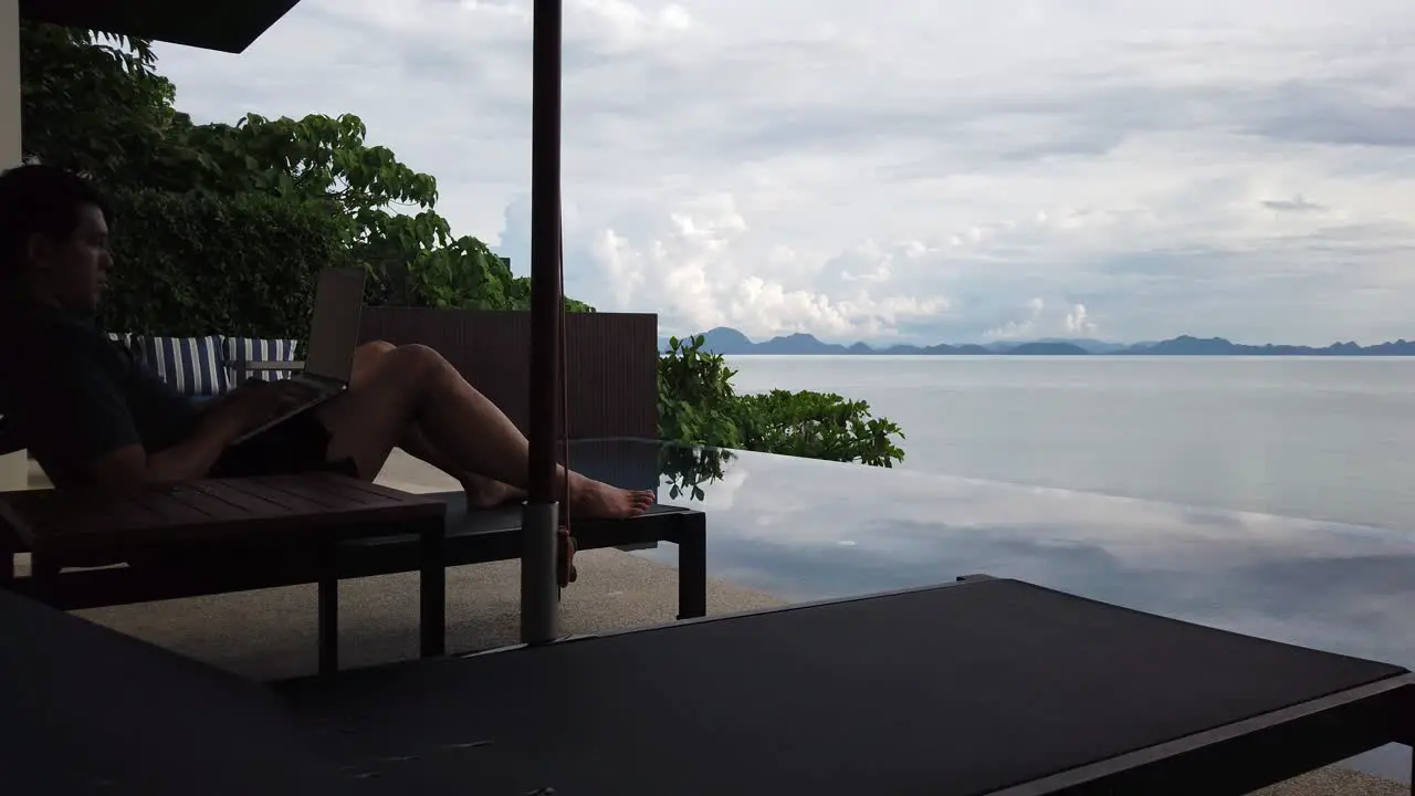 Asian man working on the laptop by the pool back view