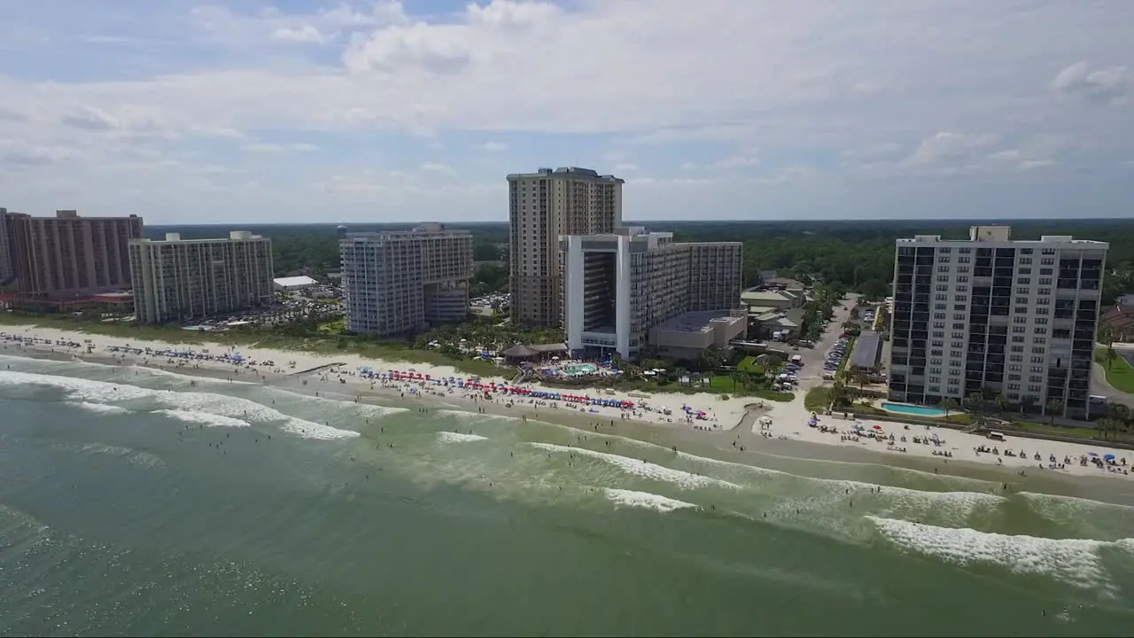 Dolly shot of drone slowly descending above ocean looking towards ocean front resorts