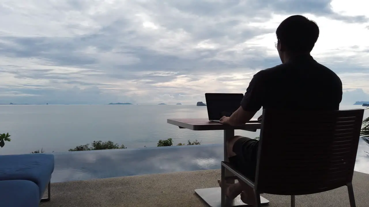 Asian man working on the laptop by the pool back view 2