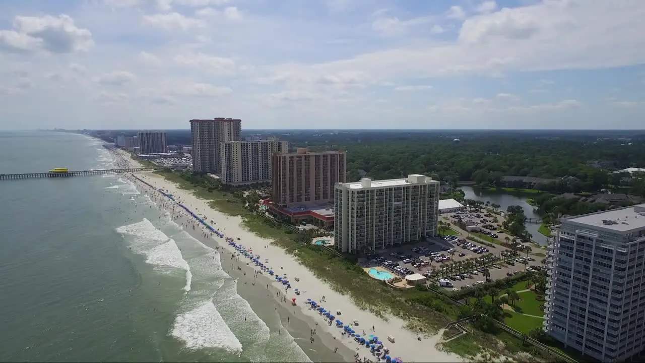 Drone flying away from beach and ocean front resorts over the ocean on sunny day