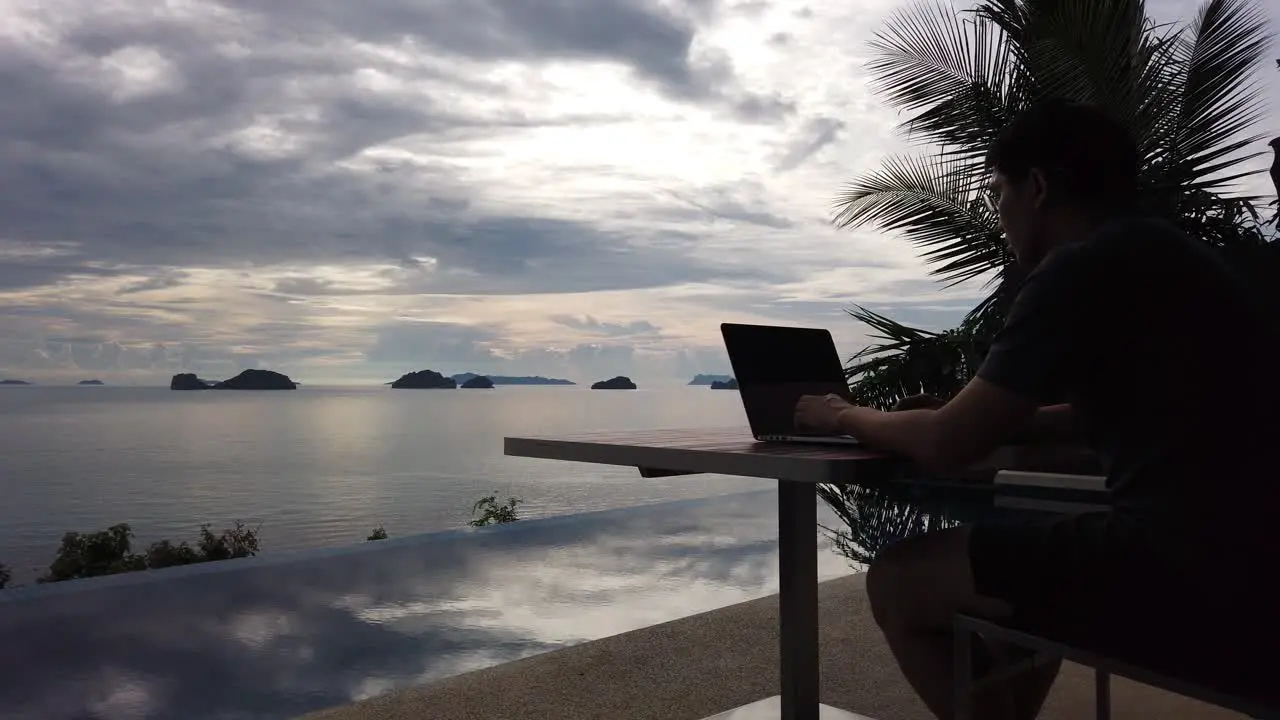 Asian man working on the laptop by the pool side view