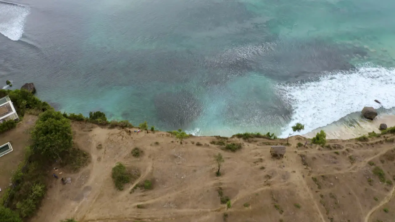 Fly drone backward above Indian Ocean filming big waves and Dreamland beach hill in Bali Indonesia