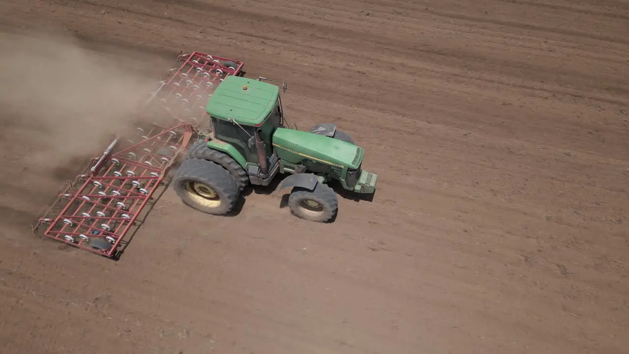 Aerial Dust rises as tractor pulls spring harrow through field soil