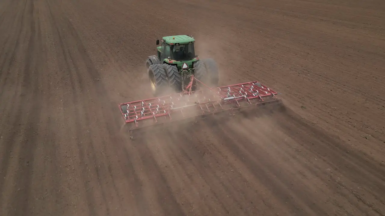 Green tractor pulls tine harrow during agriculture seeding in field