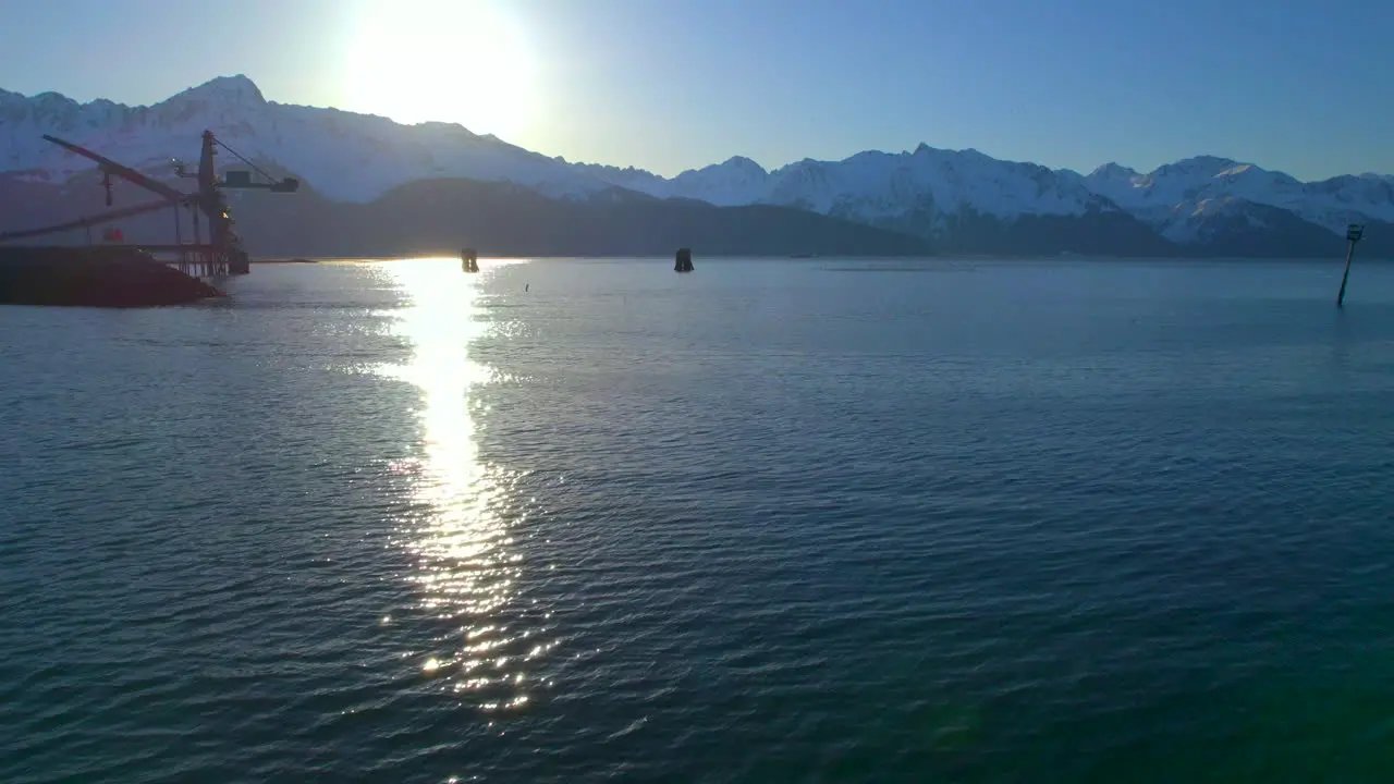 Drone flying over water towards mountains and sunrise in Seward Alaska