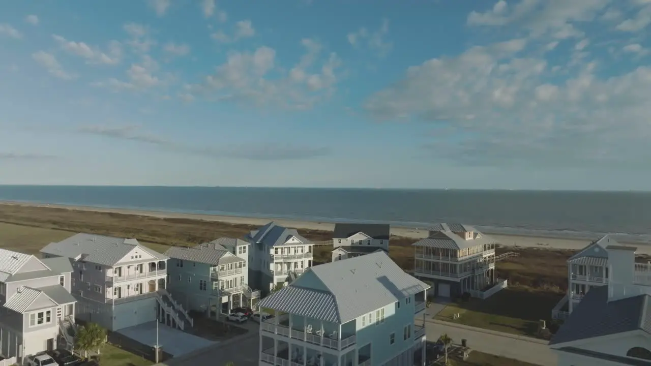 An aerial view of beach houses overlooks Galveston Beach set against a backdrop of blue skies and white clouds on East Beach in Galveston Island Texas