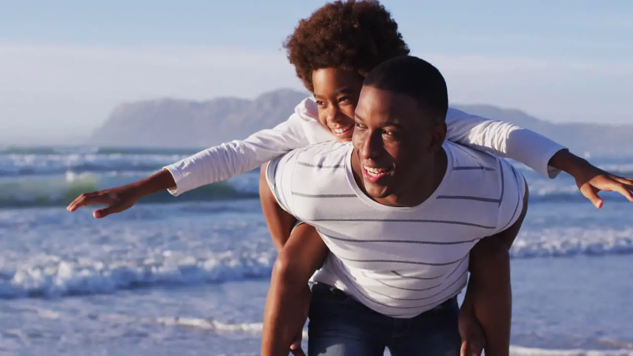 African american father giving a piggyback ride to his son at the beach