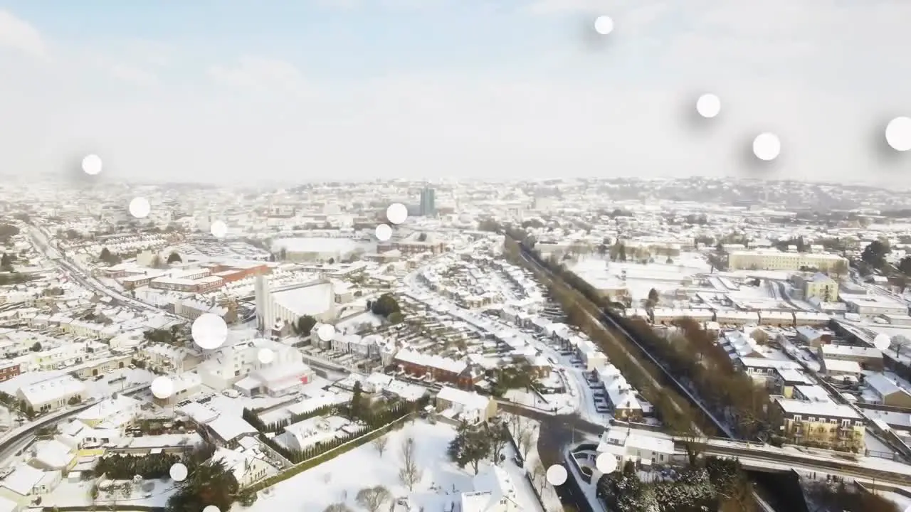 Digital composition of multiple white spots floating against aerial view of snow covered cityscape