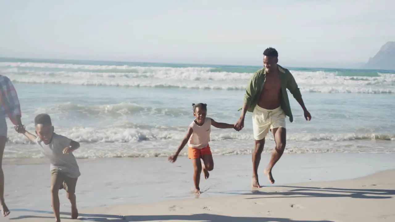 African american family holding hands running together on the beach