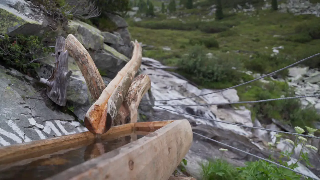 A wooden fountain in the foreground and a river running down a mountain in the background