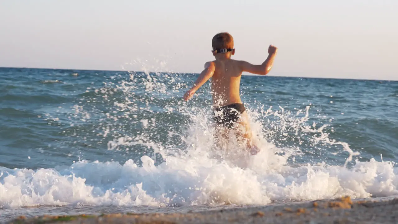 Child enjoying vacation on the coast and running into sea to swim