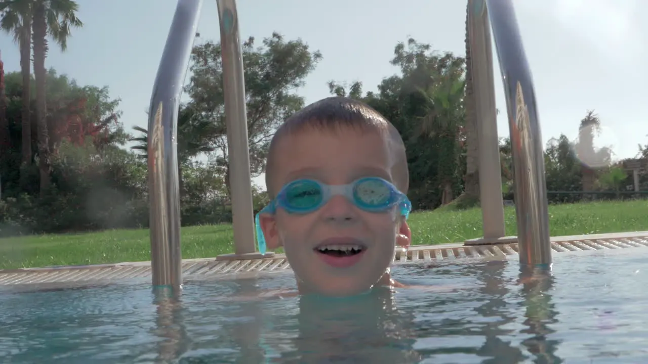 Cheerful child in goggles bathing in outdoor swimming pool