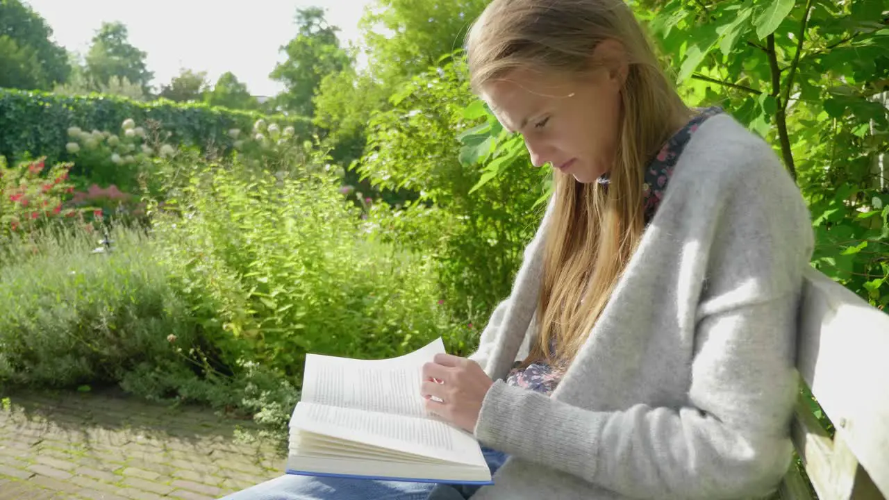 Slow motion medium shot from the side of an attractive young woman reading and studying in a lush green garden environment turning pages