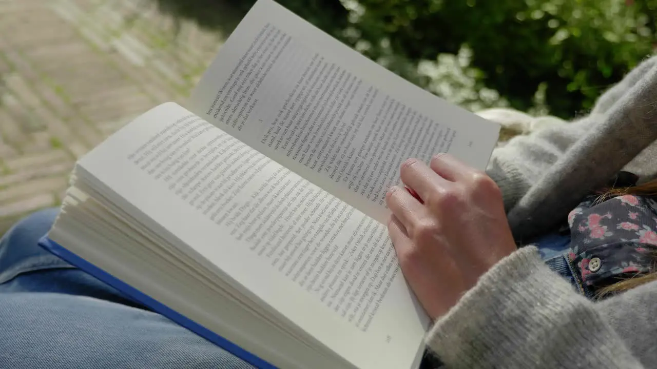 Slow motion close up shot of a book being read and by a young woman sitting turning a page