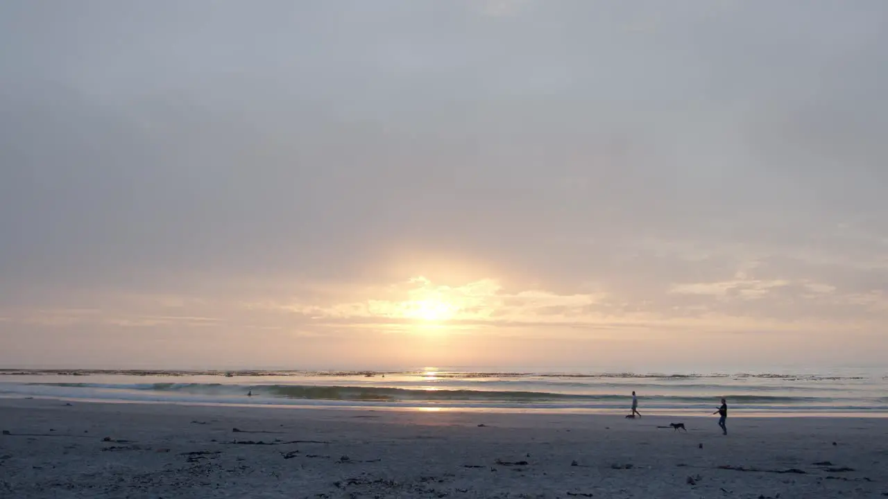 Cloudy sunrise on the beach as people walk their dogs in peace