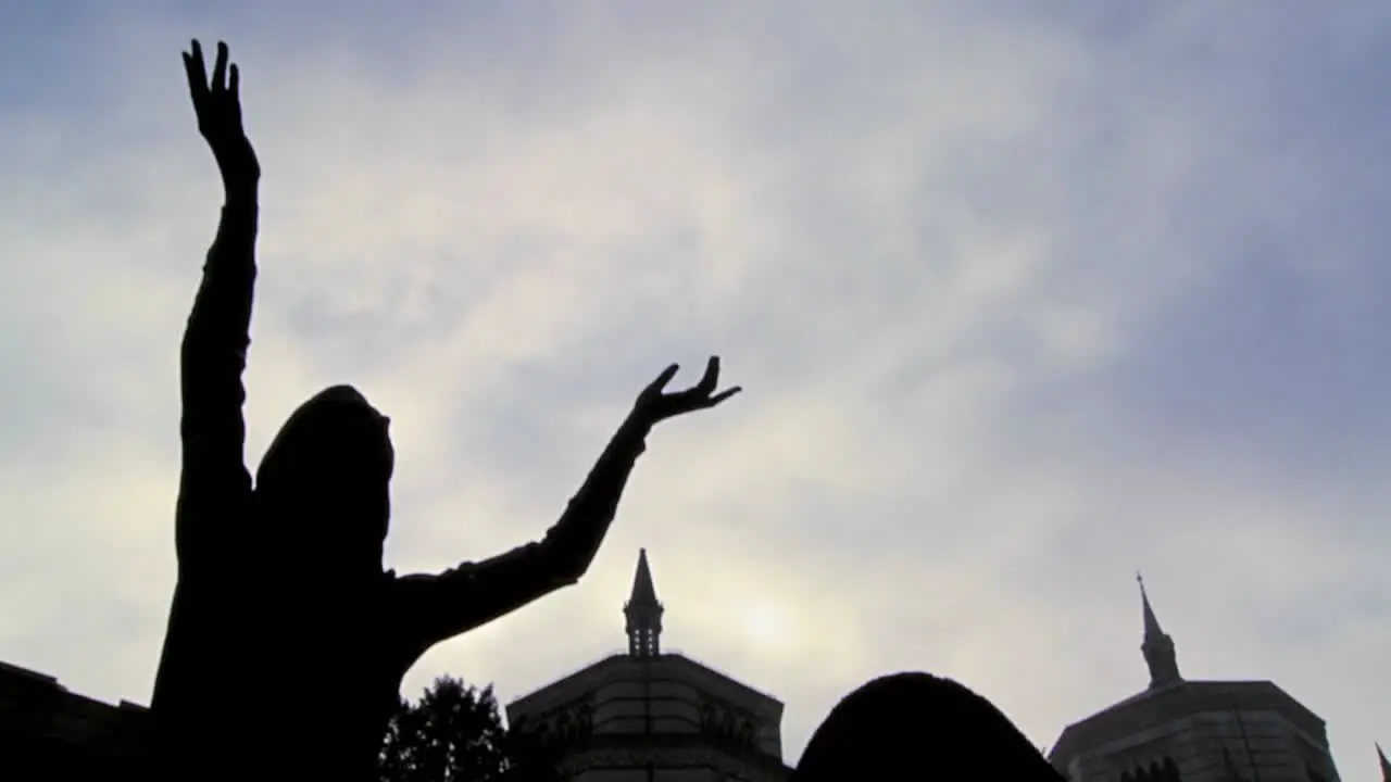 Clouds sweep over a statue in a cemetery in time lapse which seems to be appealing to the heavens for mercy