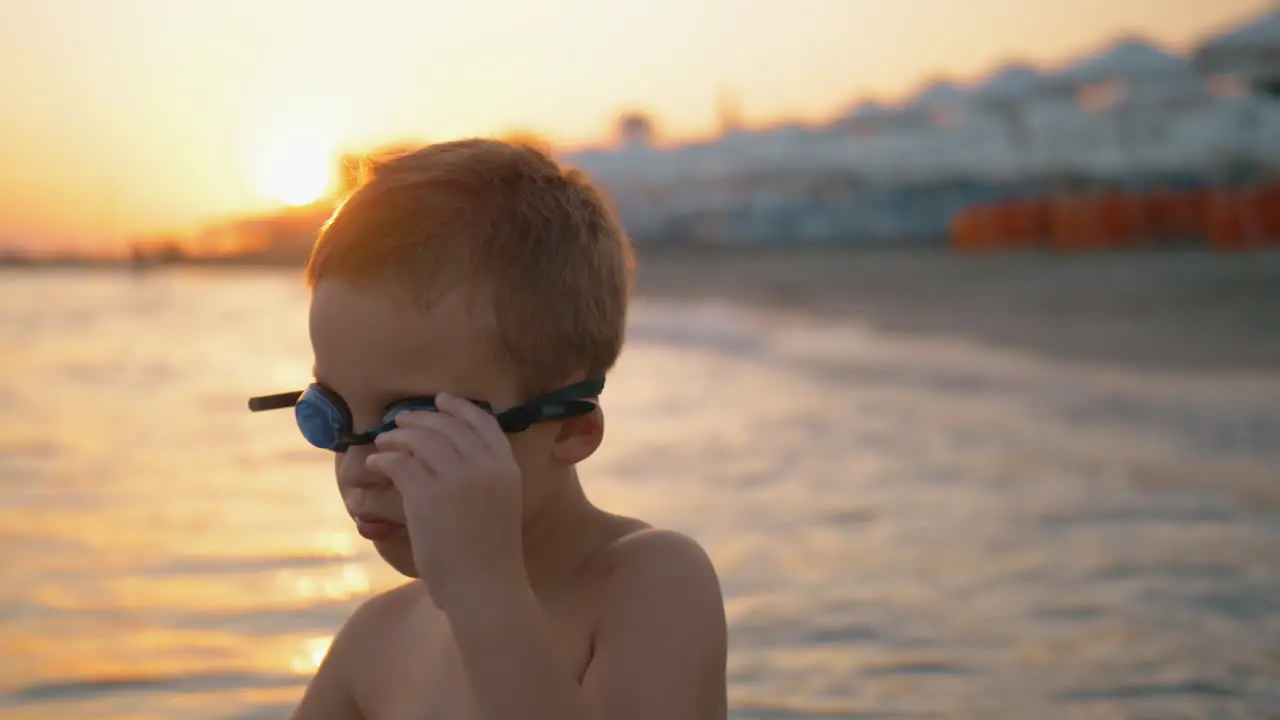 Child in goggles is going to bathe at sunset