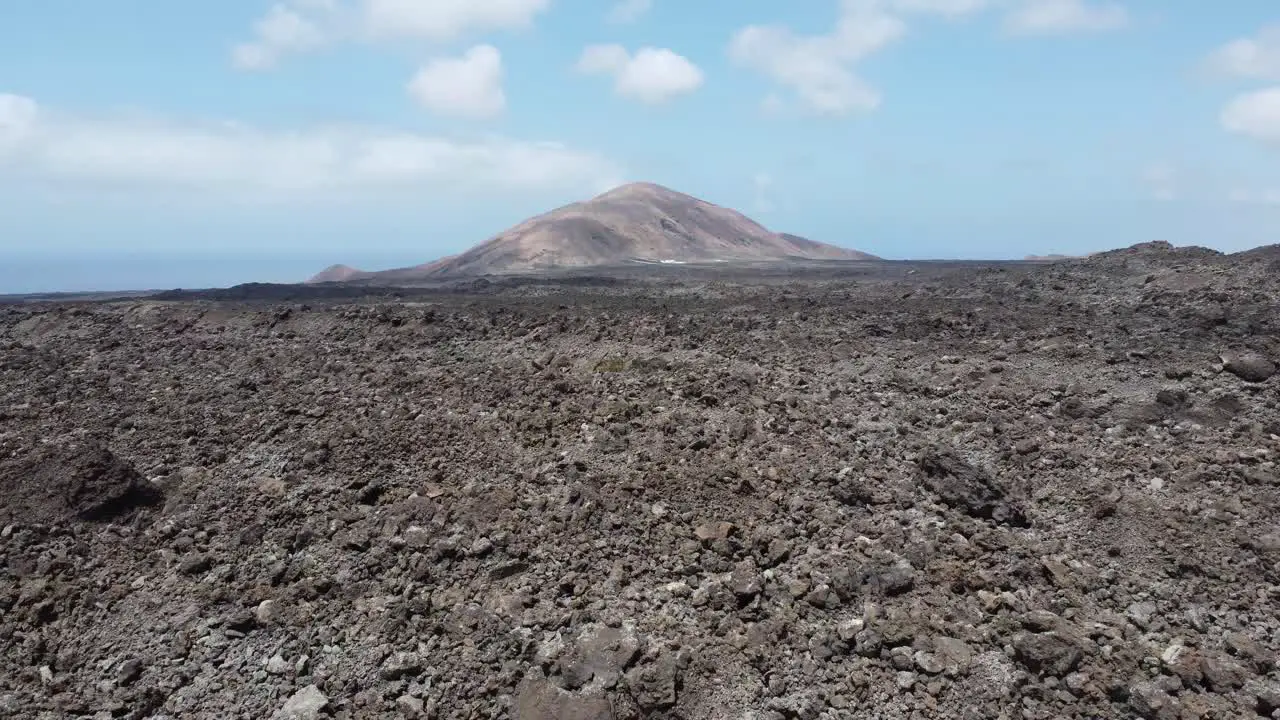 drone flies over dry lava field with a volcano crater in the background island of lanarote sunny weather