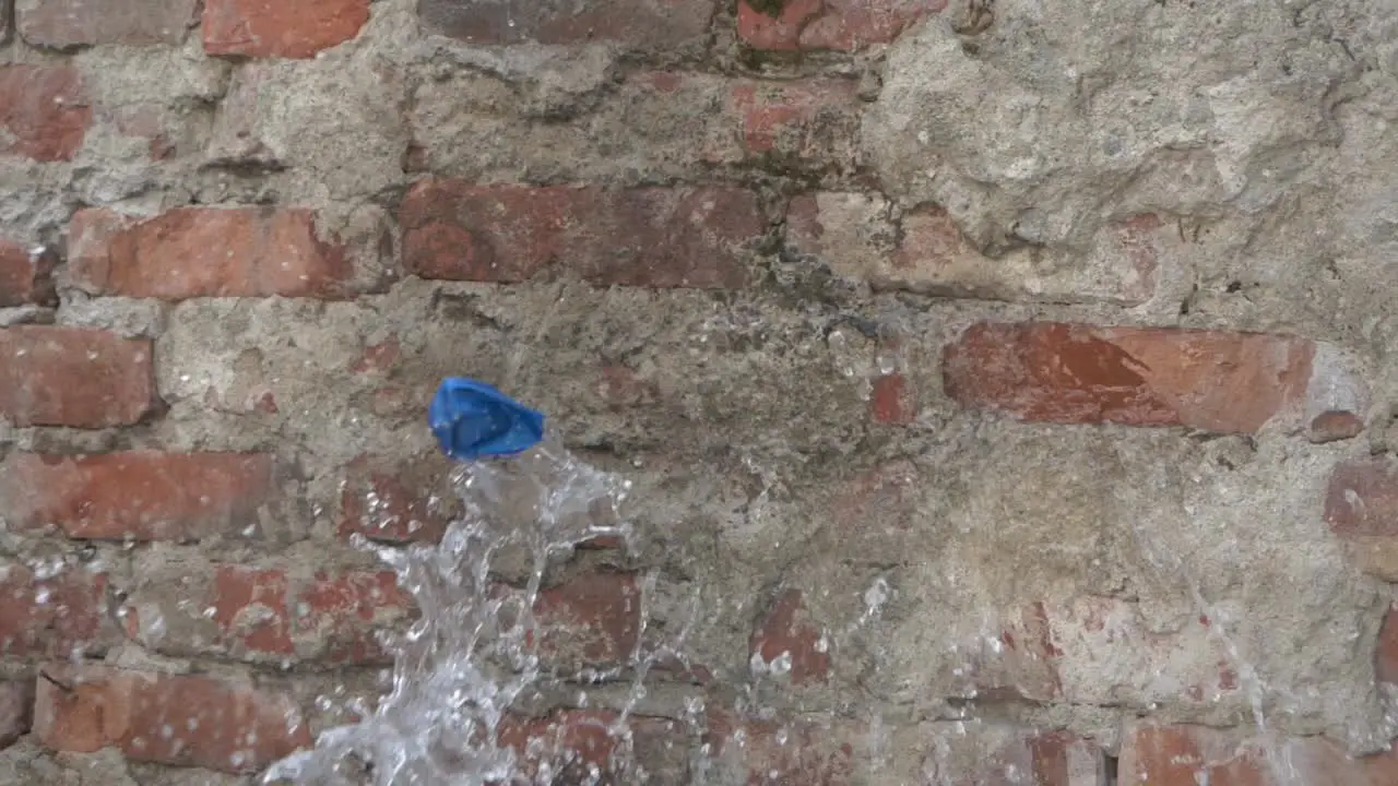 Blue Rubber Water Balloon Gets Thrown At A Brick Wall And Pops