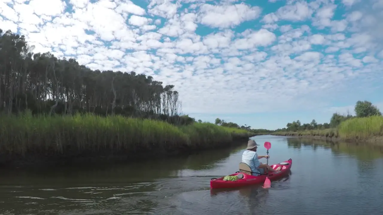 Slow motion shot following a man paddling down a river in a red kayak