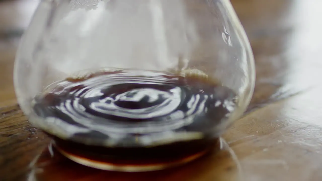 A brown liquid is dripping into a large glass container