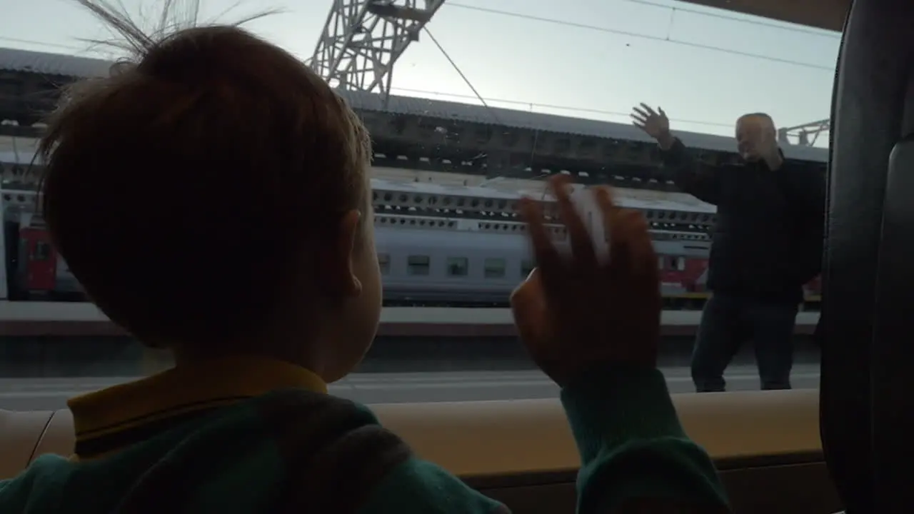 Child in train waving hand to grandparents as he leaving