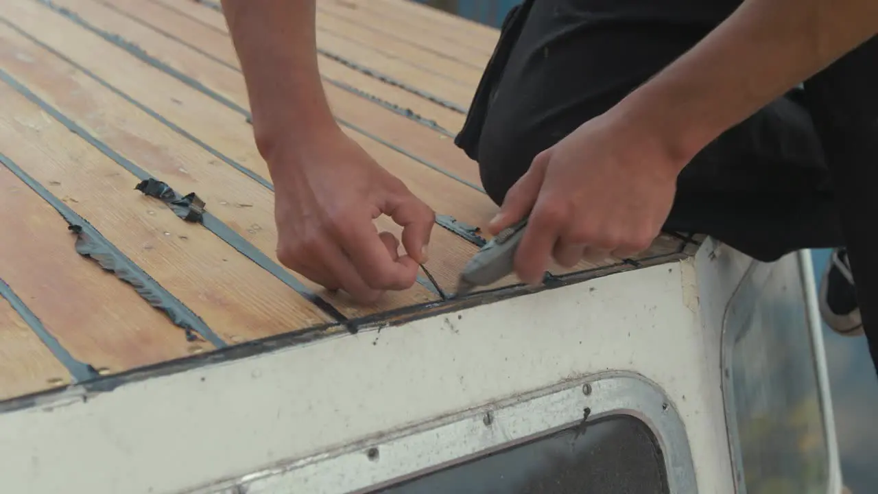 Trimming sika flex mastic flashing sealant at edge of cabin wooden boat