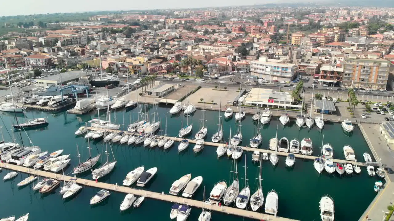 Aerial tilt down reveal marina full of boats next to modern mediterranean town