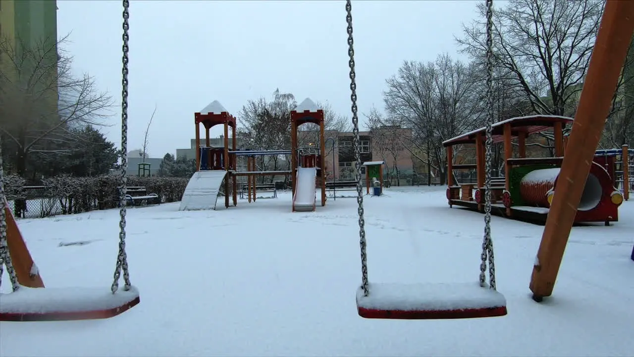 Snow is falling at a small playground in the city