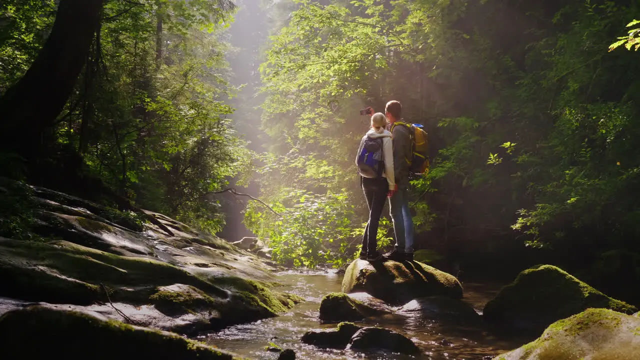 A Pair Of Travelers Are Photographed In A Picturesque Place In A Forest Near A Mountain River 4K Vid