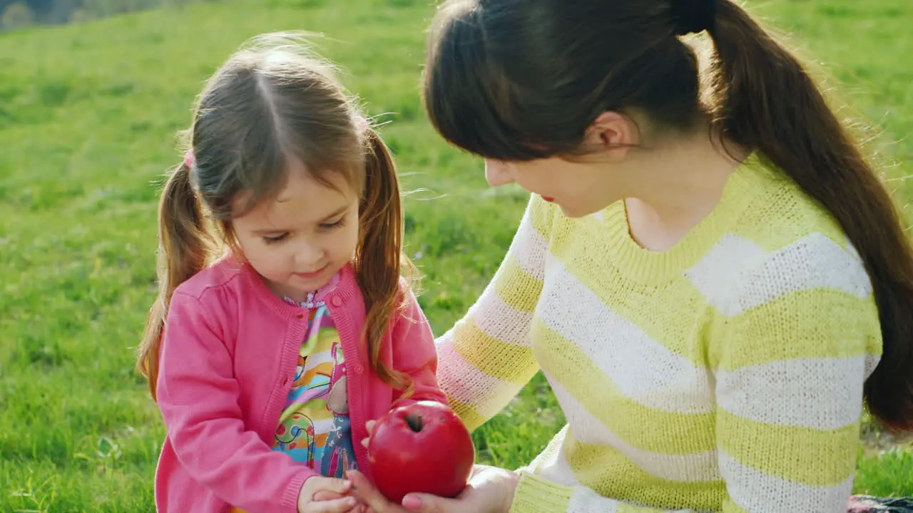 Funny Child Enjoys Nature Together With A Young Mother Playing With A Red Apple Against A Background